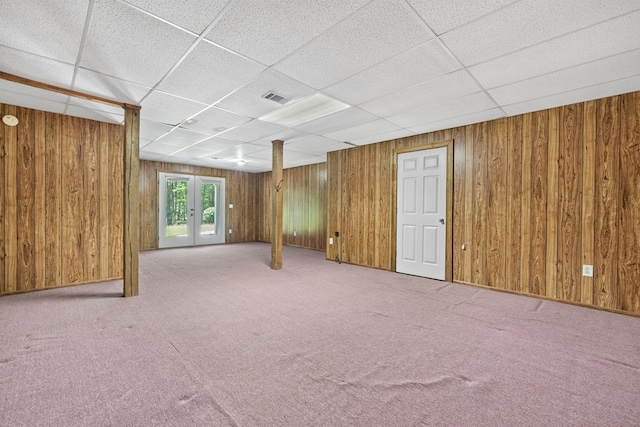 unfurnished living room featuring wooden walls, carpet floors, a drop ceiling, and visible vents