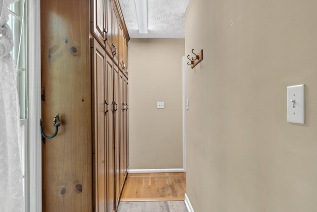 hall with light wood-style floors, baseboards, and a textured ceiling