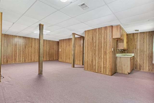 finished basement with wooden walls, visible vents, and a drop ceiling