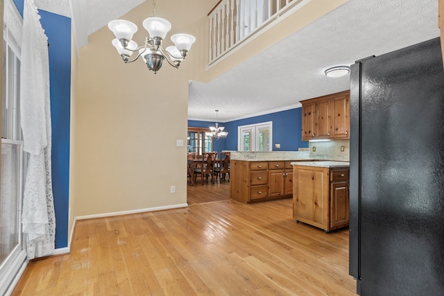 kitchen featuring an inviting chandelier, freestanding refrigerator, a kitchen island, light countertops, and light wood-style flooring