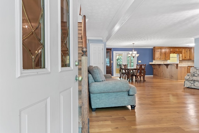 entryway featuring a textured ceiling, a notable chandelier, ornamental molding, and light wood-style floors
