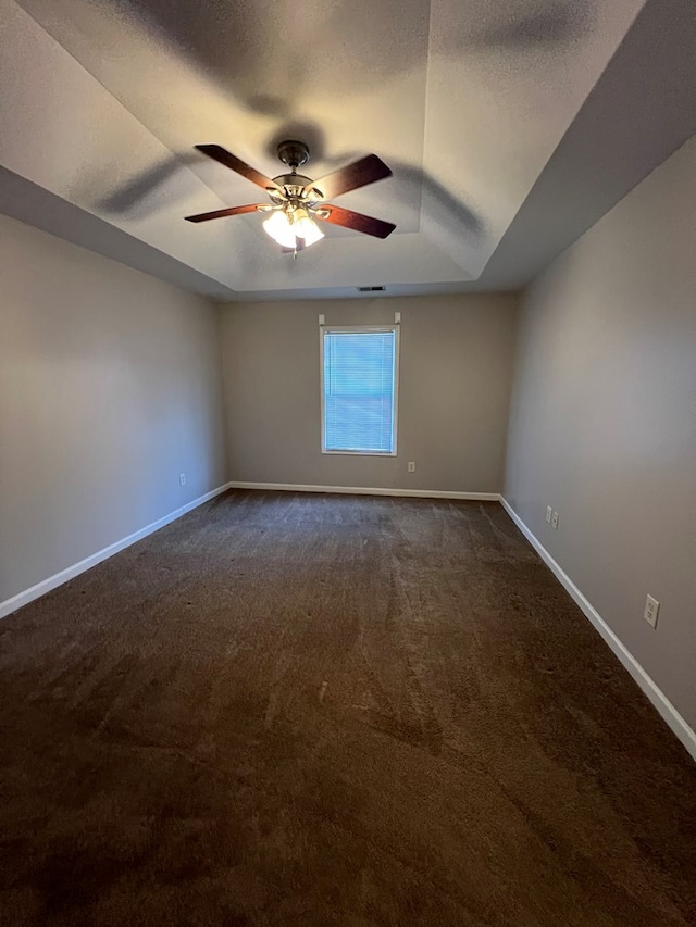 spare room featuring a raised ceiling, dark colored carpet, ceiling fan, and a textured ceiling