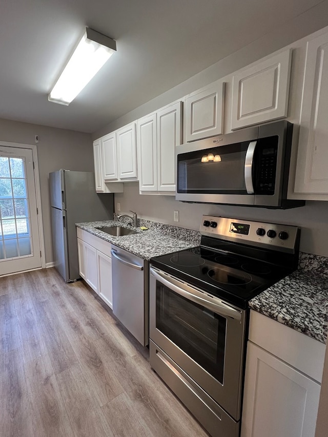 kitchen featuring appliances with stainless steel finishes, light wood-type flooring, light stone countertops, white cabinets, and sink