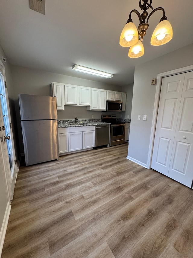 kitchen with stainless steel appliances, white cabinets, sink, and a notable chandelier