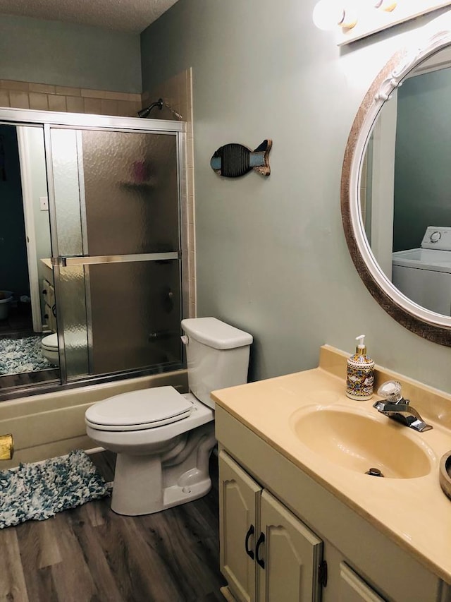 full bathroom with washer / dryer, enclosed tub / shower combo, hardwood / wood-style floors, a textured ceiling, and toilet