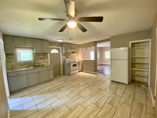 kitchen featuring under cabinet range hood, white appliances, gray cabinetry, and a sink