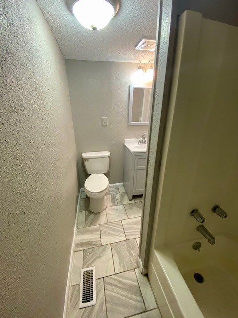 full bathroom with visible vents, toilet, a textured ceiling, vanity, and a textured wall