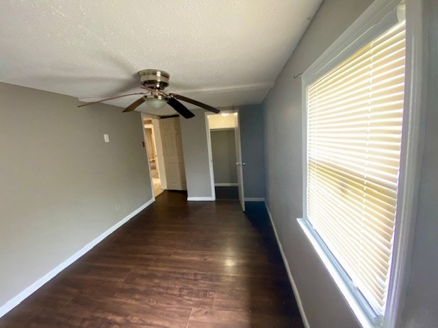 empty room with baseboards, a textured ceiling, ceiling fan, and dark wood-type flooring