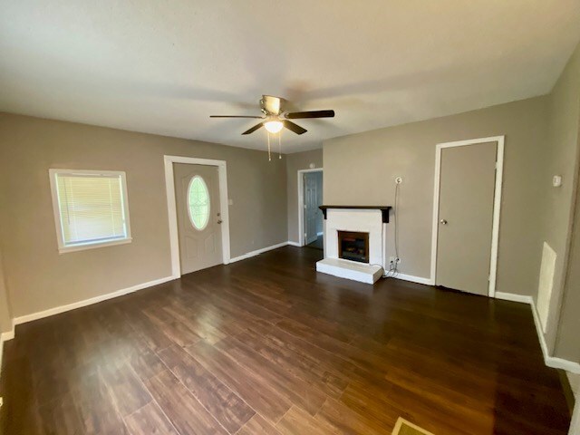 unfurnished living room featuring a fireplace with raised hearth, ceiling fan, baseboards, and wood finished floors