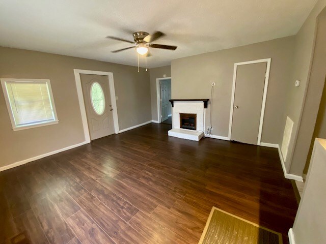 unfurnished living room with ceiling fan, a fireplace, baseboards, and wood finished floors