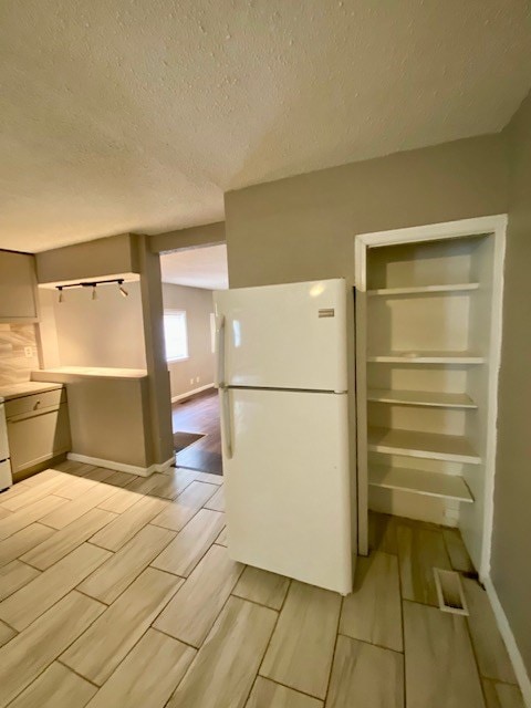 kitchen featuring a textured ceiling, freestanding refrigerator, light countertops, baseboards, and wood tiled floor