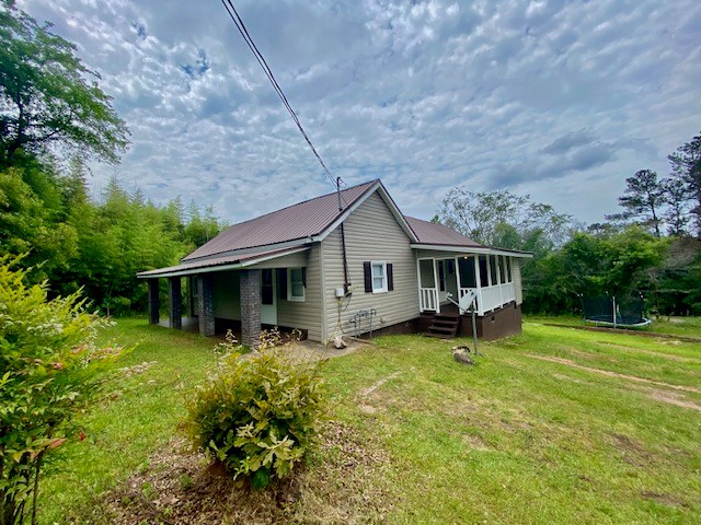 view of side of home featuring metal roof, a trampoline, a lawn, and a sunroom