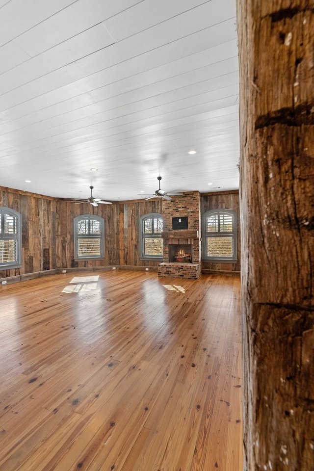 unfurnished living room with a healthy amount of sunlight, a stone fireplace, wood-type flooring, and ceiling fan