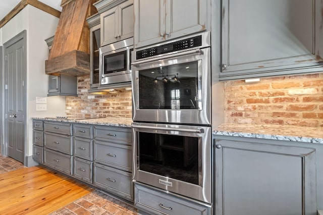 kitchen featuring light stone countertops, appliances with stainless steel finishes, gray cabinetry, and decorative backsplash