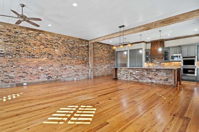 unfurnished living room with brick wall, sink, ceiling fan, and light hardwood / wood-style floors