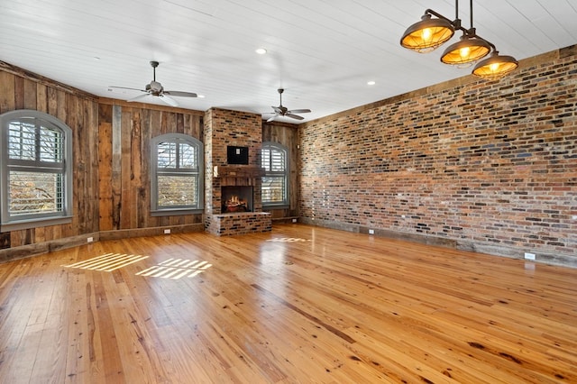 unfurnished living room with wooden ceiling, light wood-type flooring, ceiling fan, brick wall, and a fireplace