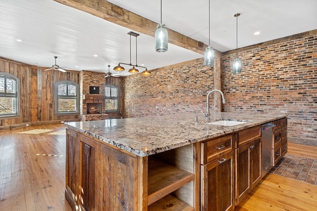 kitchen with pendant lighting, sink, a kitchen island with sink, and light wood-type flooring