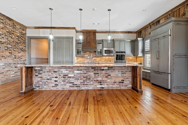 kitchen featuring built in appliances, hanging light fixtures, light stone countertops, and light wood-type flooring