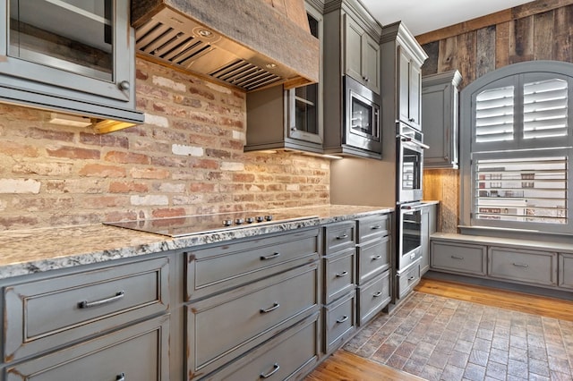 kitchen featuring light stone counters, stainless steel appliances, custom range hood, and gray cabinetry