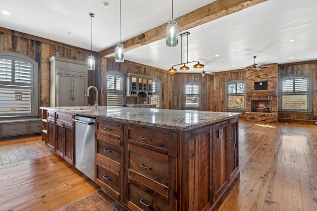 kitchen with a fireplace, wood walls, wood-type flooring, hanging light fixtures, and a center island with sink