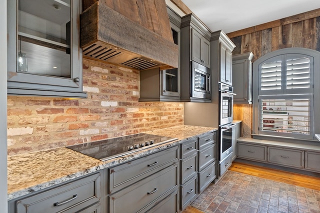 kitchen with custom exhaust hood, light stone countertops, and appliances with stainless steel finishes