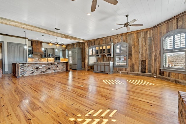 unfurnished living room featuring sink, beam ceiling, light hardwood / wood-style flooring, and ceiling fan