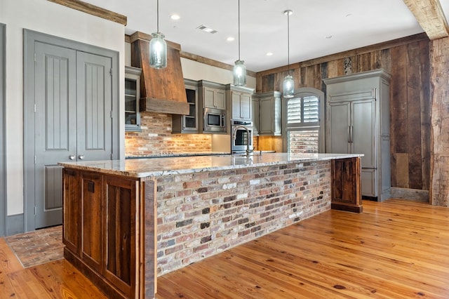 kitchen with a spacious island, built in appliances, light stone countertops, and pendant lighting