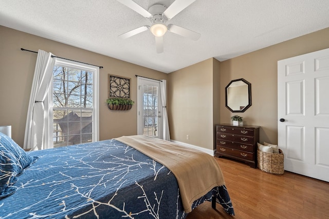 bedroom with baseboards, a ceiling fan, a textured ceiling, wood finished floors, and access to exterior