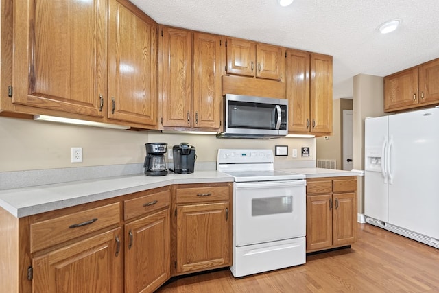 kitchen with light wood-type flooring, white appliances, light countertops, a textured ceiling, and brown cabinetry