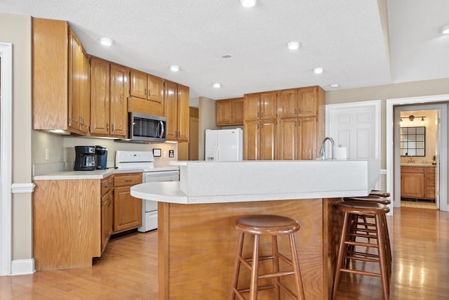 kitchen featuring white appliances, light countertops, light wood-style floors, a breakfast bar area, and a sink