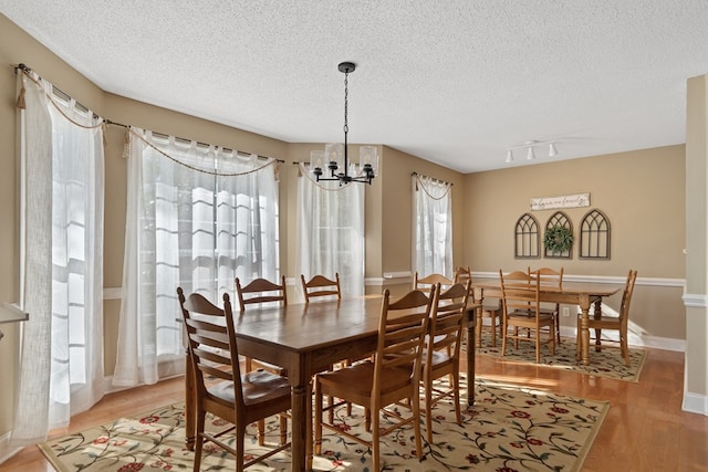 dining space with rail lighting, a notable chandelier, light wood-style floors, and a textured ceiling