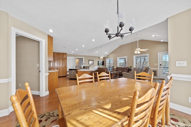 dining area featuring light wood-style floors, ceiling fan with notable chandelier, vaulted ceiling, and a wealth of natural light