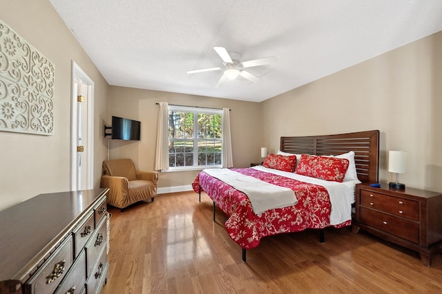 bedroom with ceiling fan, light wood-type flooring, baseboards, and a textured ceiling