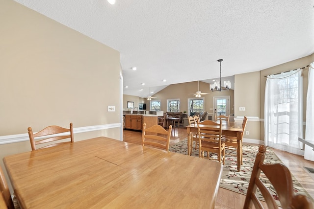 dining space featuring baseboards, vaulted ceiling, light wood-style flooring, a textured ceiling, and ceiling fan with notable chandelier