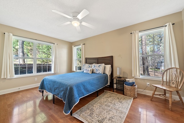 bedroom featuring wood finished floors, ceiling fan, baseboards, and multiple windows