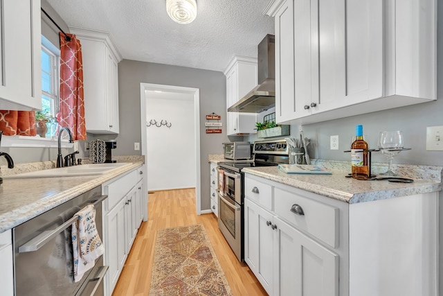 kitchen with sink, wall chimney exhaust hood, a textured ceiling, white cabinetry, and stainless steel appliances