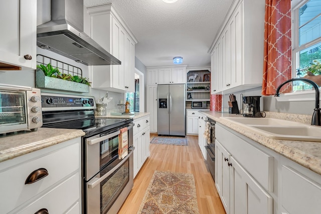 kitchen featuring white cabinets, wall chimney range hood, sink, light hardwood / wood-style floors, and stainless steel appliances