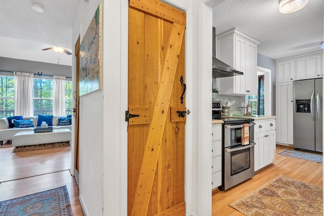 kitchen with appliances with stainless steel finishes, light wood-type flooring, a textured ceiling, ceiling fan, and white cabinetry