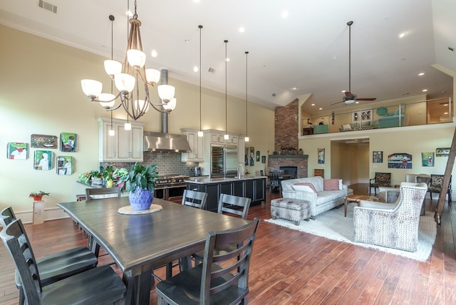 dining area featuring a high ceiling, ceiling fan with notable chandelier, dark hardwood / wood-style floors, and a stone fireplace