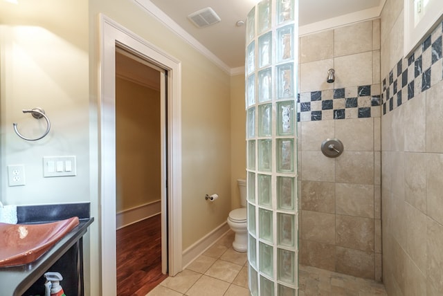 bathroom with tile patterned floors, toilet, crown molding, and tiled shower