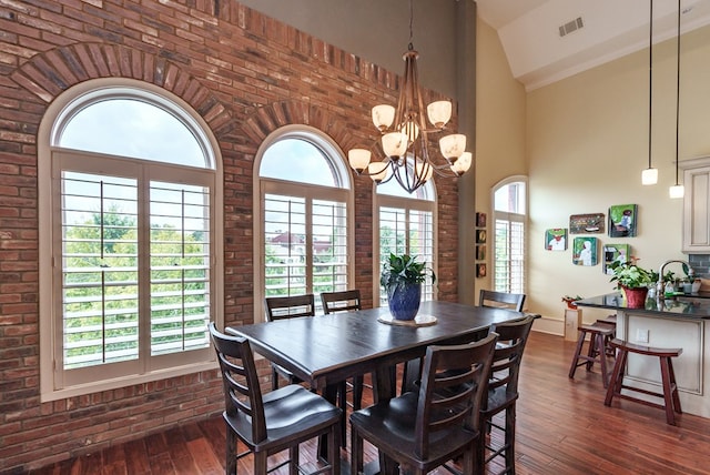 dining area with high vaulted ceiling, dark wood-type flooring, brick wall, and an inviting chandelier