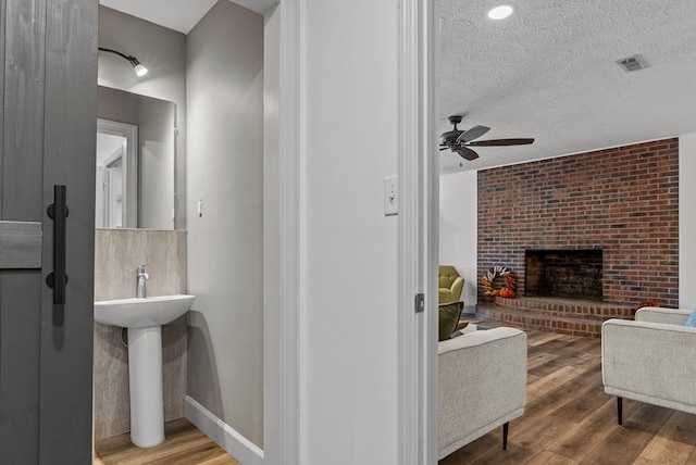 bathroom with a fireplace, ceiling fan, wood-type flooring, and a textured ceiling