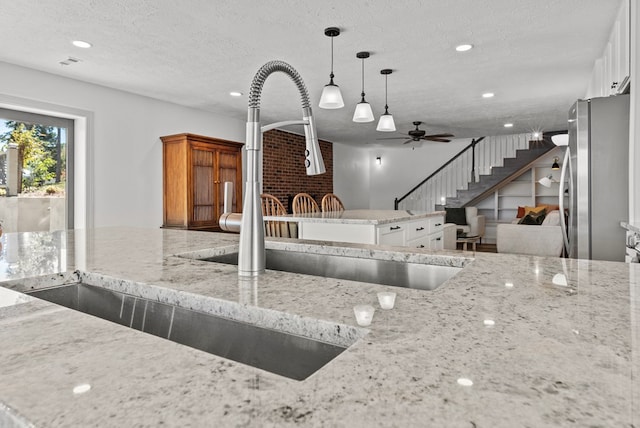 kitchen with light stone countertops, white cabinetry, hanging light fixtures, and stainless steel refrigerator