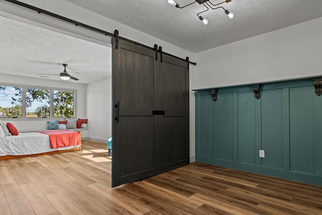 unfurnished bedroom with wood-type flooring, a textured ceiling, ceiling fan, and a barn door