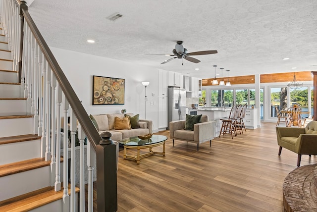 living room featuring a textured ceiling, light hardwood / wood-style flooring, and ceiling fan with notable chandelier