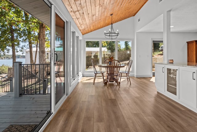 unfurnished sunroom featuring a water view, vaulted ceiling, a notable chandelier, wood ceiling, and beverage cooler