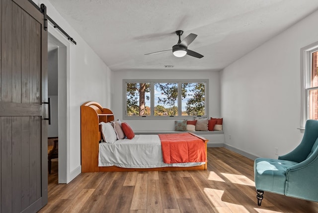 bedroom with ceiling fan, a barn door, wood-type flooring, and a textured ceiling