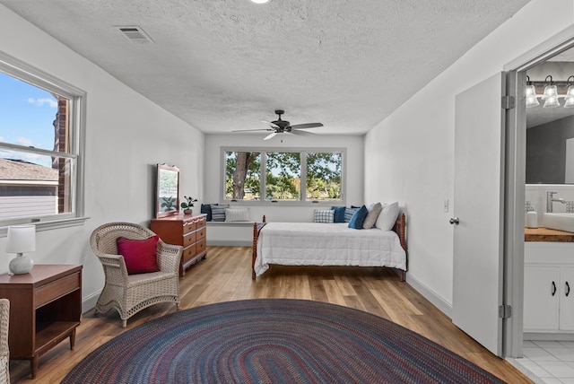 bedroom with ensuite bathroom, light hardwood / wood-style flooring, ceiling fan, and a textured ceiling