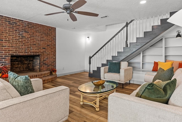 living room featuring hardwood / wood-style floors, a textured ceiling, a brick fireplace, and ceiling fan