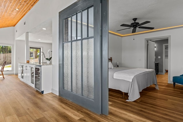 bedroom with wood ceiling, a textured ceiling, ceiling fan, light hardwood / wood-style flooring, and wine cooler